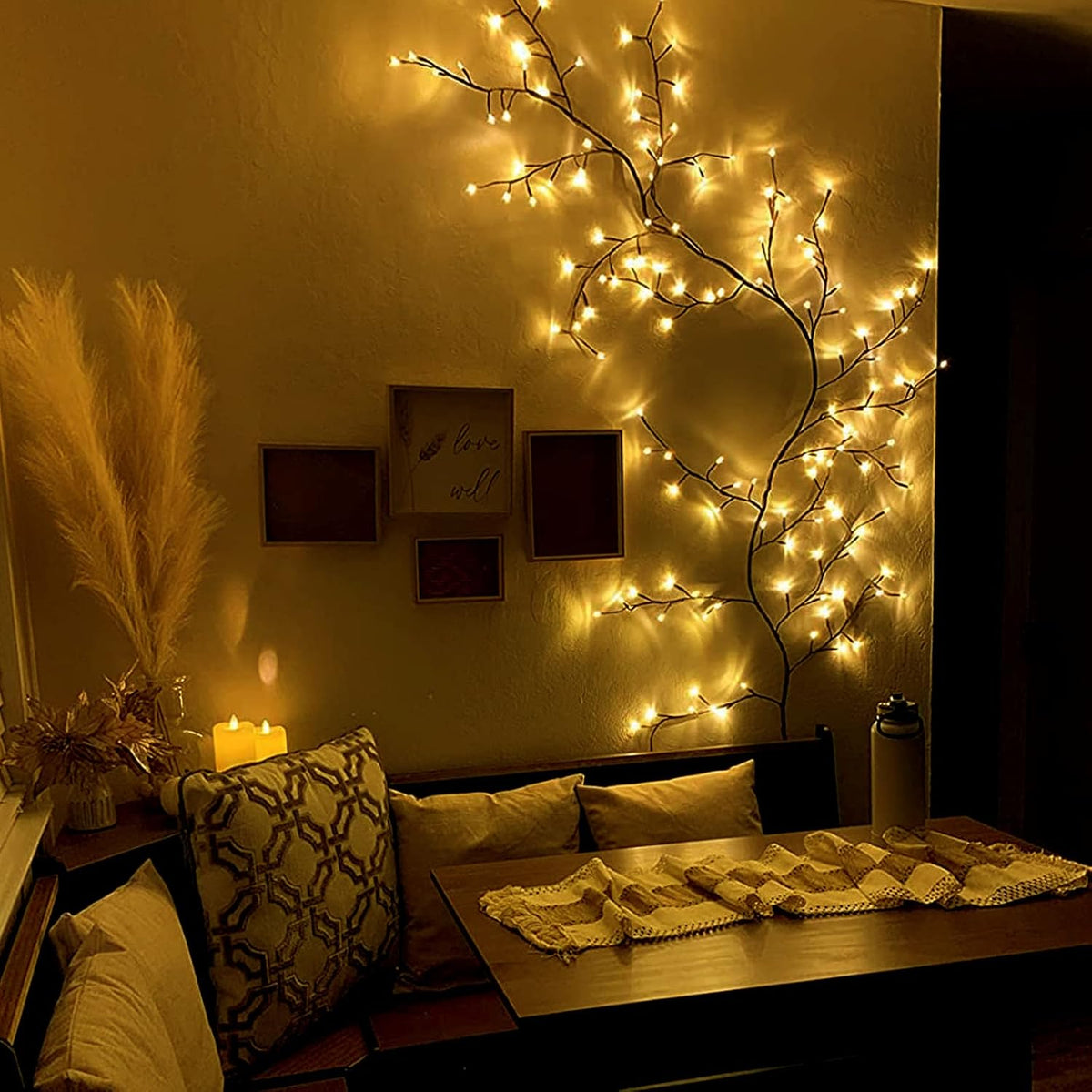 Decorative string lights on a branch in a cozy room with a table and pillows.